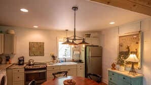A kitchen with a wooden table, a refrigerator, and a hanging light fixture.