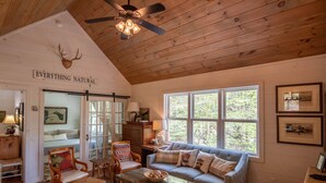A cozy room with a large window, a ceiling fan, a sofa with cushions, and a wooden floor.