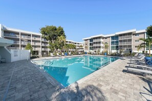 Une piscine entourée de chaises longues et un immeuble à plusieurs étages doté de balcons.