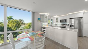 A modern kitchen with white cabinetry, a stainless steel refrigerator, and a dining area with a glass table and chairs. - Island Beach Club 330B – Gulf view vacation rental condo on Sanibel Island (Sanibel)