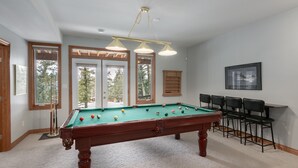 Una mesa de billar en una habitación con ventanas amplias, una lámpara en el techo e imagen enmarcada en la pared.