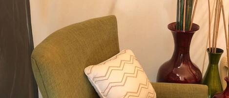 A green armchair with a zigzag patterned pillow, positioned next to a wall with two red vases and tall bamboo plants.