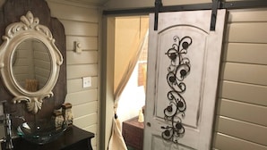 Een badkamer met een donker houten wastafelmeubel, een glazen wasbak, een decoratieve spiegel en een schuifdeur met een metalen handgreep.