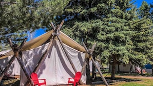 Een tent met twee rode stoelen op een houten terras, omringd door bomen.