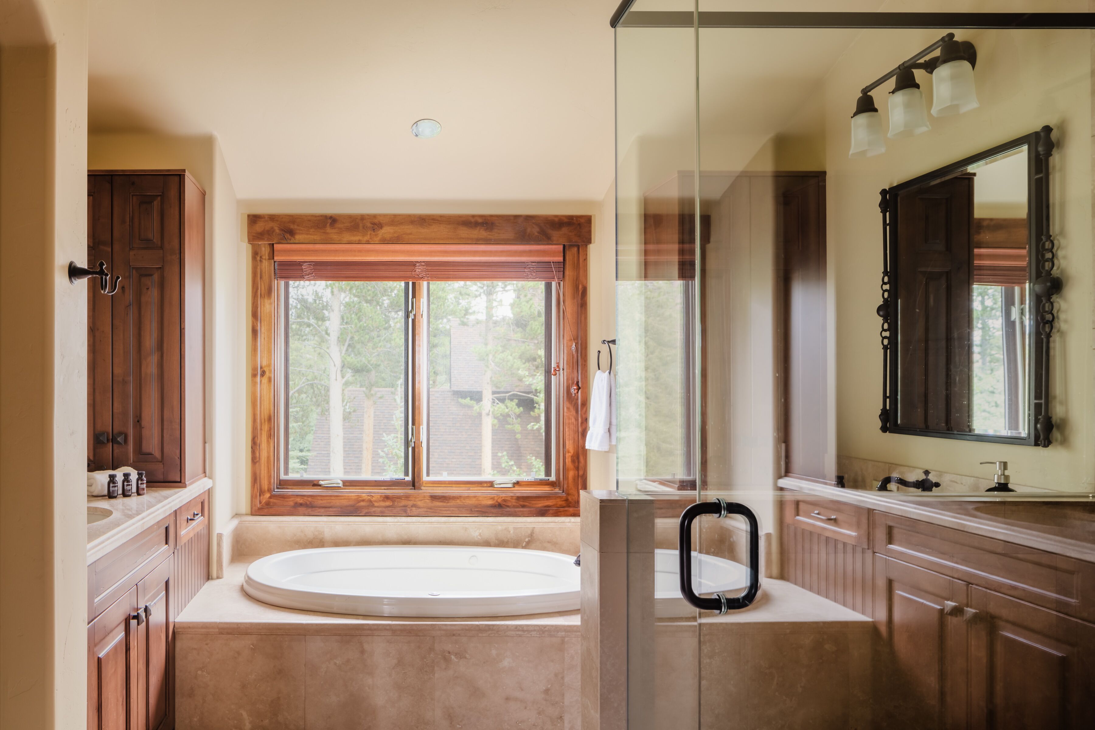 A bathroom with a large bathtub, wooden cabinets, a glass shower enclosure, and a window providing natural light.
