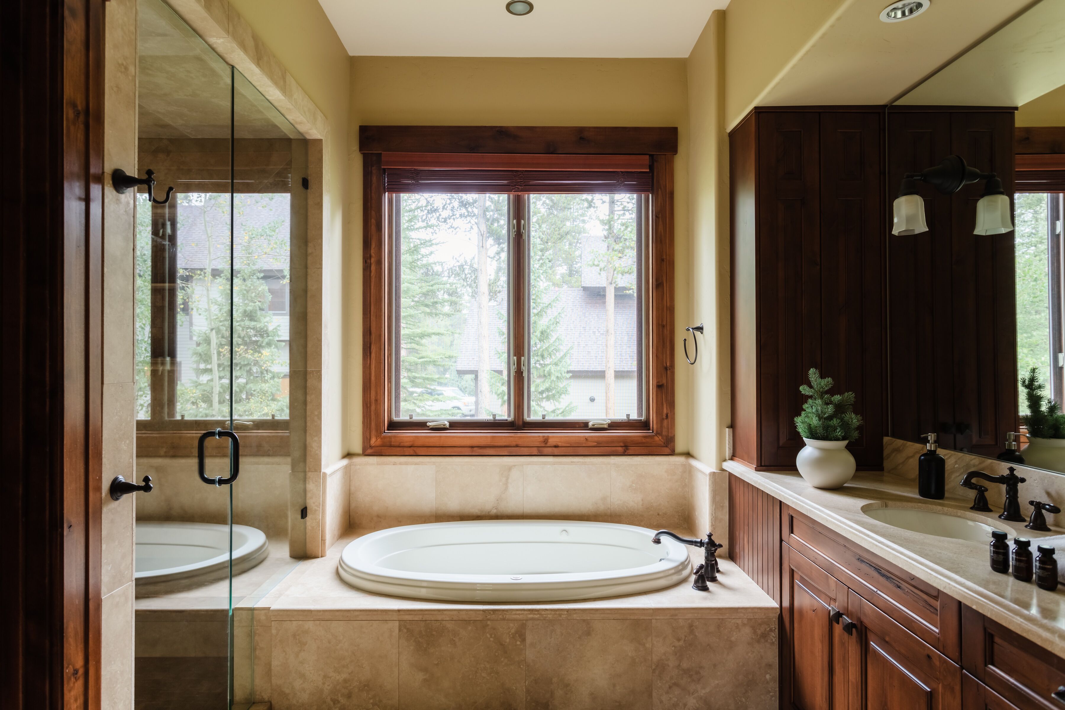 A bathroom with a large bathtub, two sinks, and a window with a view of greenery.