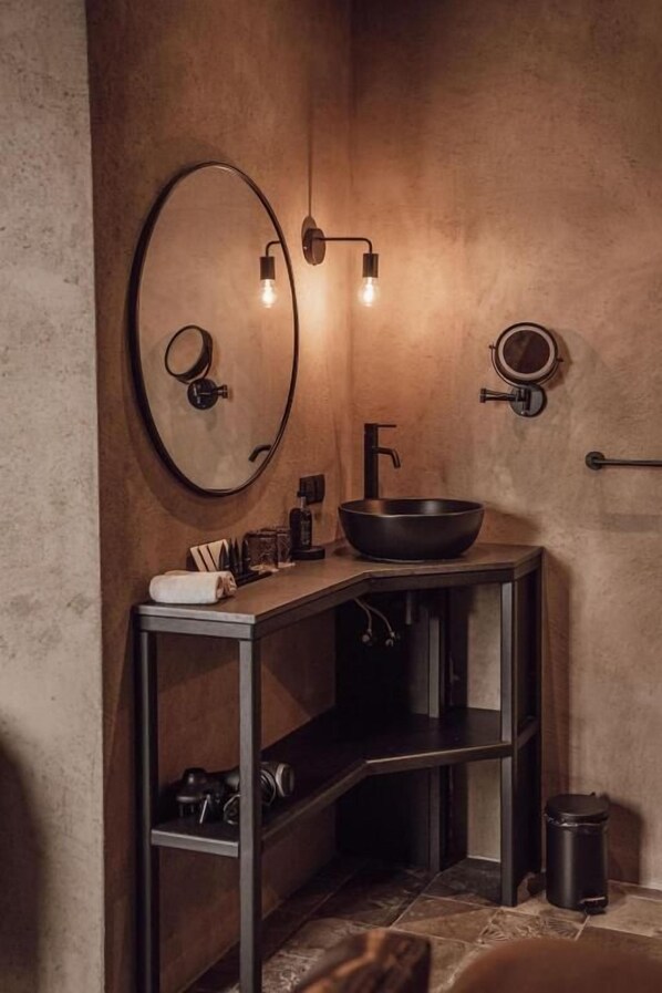 Un baño con un espejo redondo, un lavabo negro y una toalla sobre el mostrador.