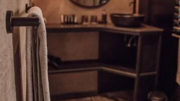 Un baño con un espejo redondo, un perchero, un lavabo y un cubo de basura.