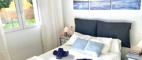 A bedroom with a bed, two pillows, a nightstand with a lamp, and a window with curtains.