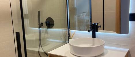 Een moderne badkamer met een douchecabine van glas, een wit wastafelmeubel en een houten opbergkast.