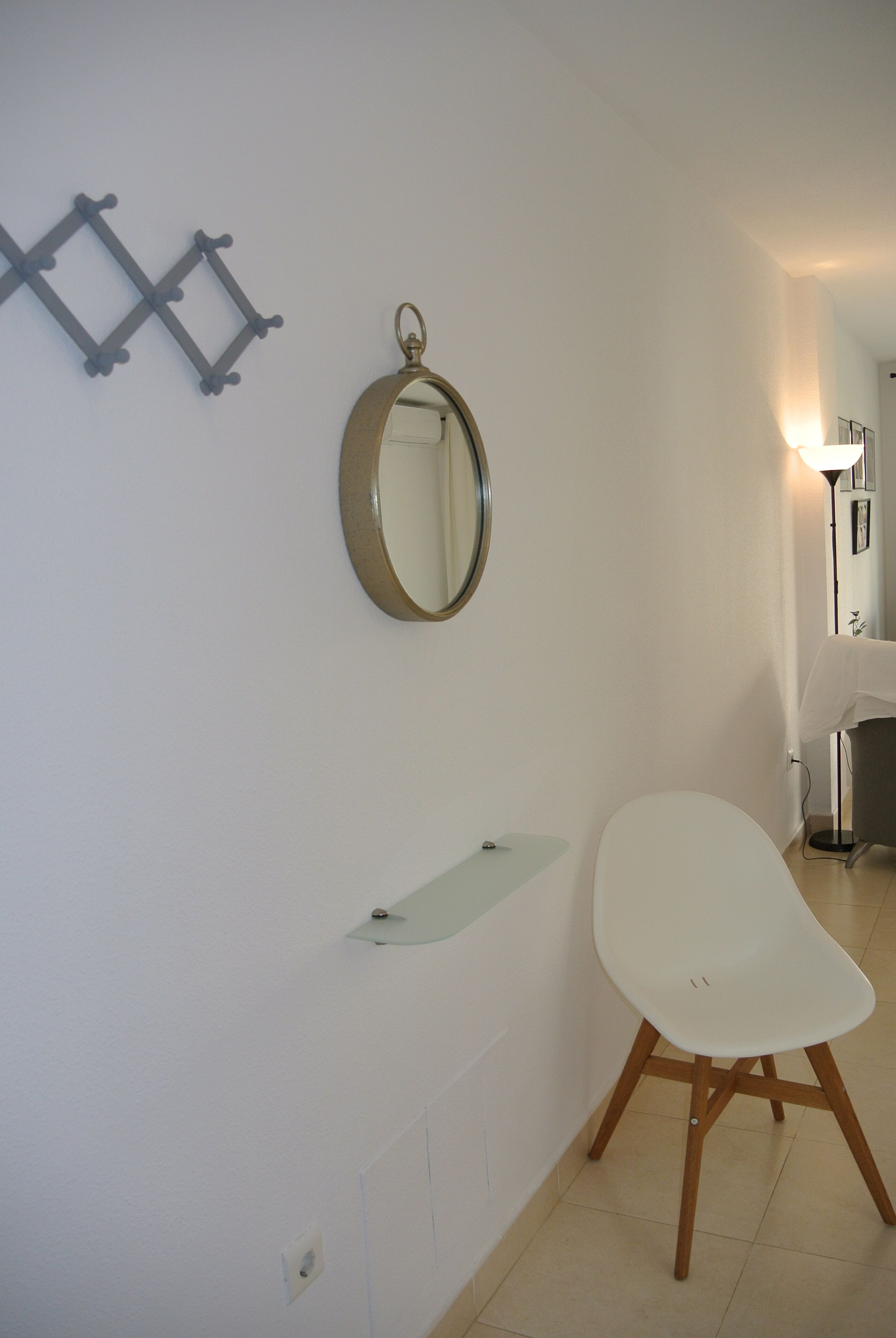 Ein Badezimmer mit einem weißen Waschbecken, einem runden Spiegel und einem weißen Stuhl.
