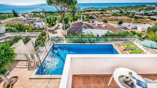 Area piscina con vista sul mare, immersa nel verde e circondata da edifici.