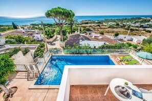 A pool area with a view of the sea, surrounded by greenery and buildings. - VILLA OCEANO | São Rafael | Albufeira - Algarve (Albufeira)