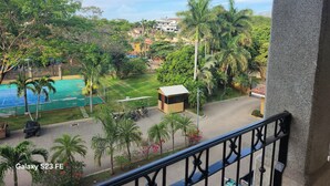 A balcony with a view of a swimming pool, palm trees, and a small building. - Spacious 3/2/ condo located minutes from downtown area of Beautiful Tamarindo  (Tamarindo)