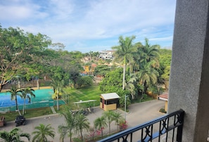 Un balcón con vista a una piscina, palmeras y un pequeño edificio.
