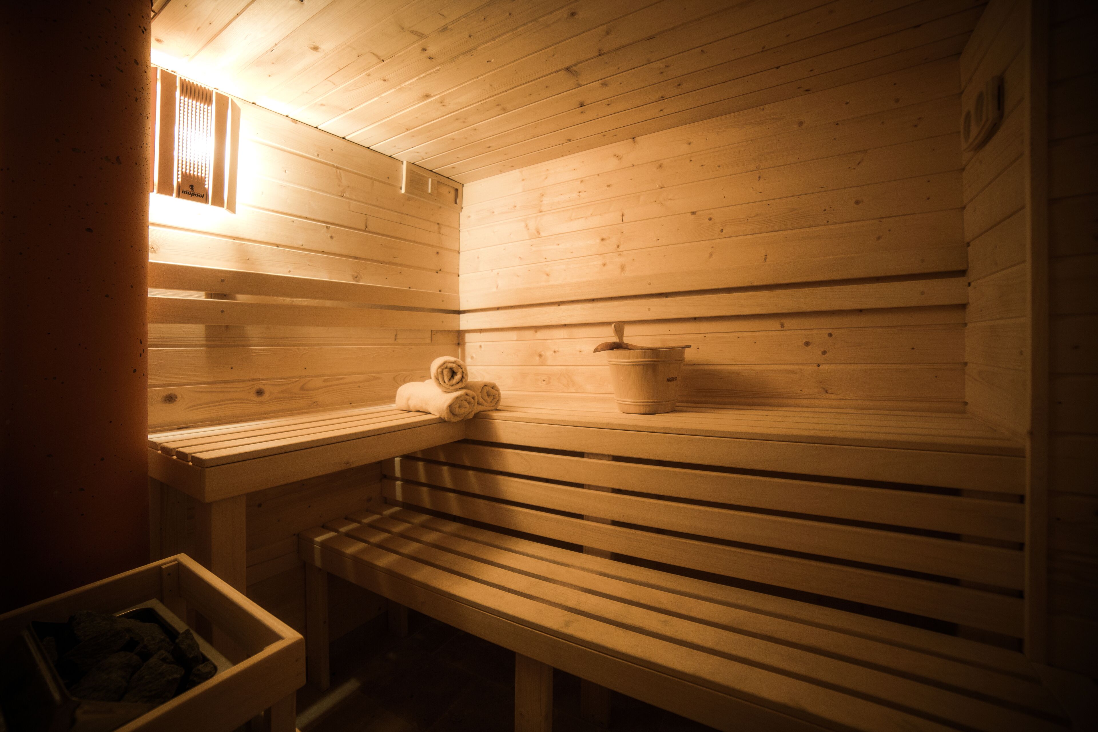 Una sauna con bancos de madera, un asiento de banco y un estante para toallas, además de un pequeño calentador.