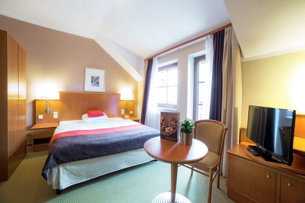A hotel room with a bed, a desk, a chair, a television, and a window with curtains.