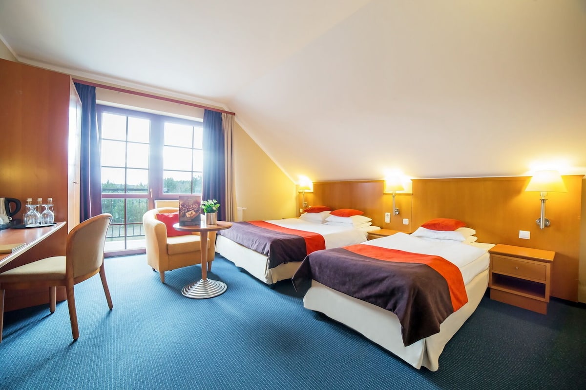A hotel room with two beds, a desk, a chair, and a small table.