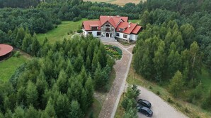 A large, two-story house with a red-tiled roof, surrounded by dense forest.