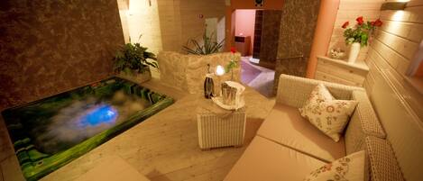 Un área de spa con hidromasaje, mobiliario de mimbre y una pared de piedra.