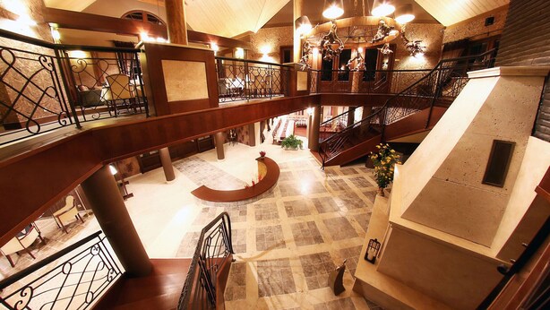 A multi-level interior with wooden beams, a grand staircase, and a chandelier.