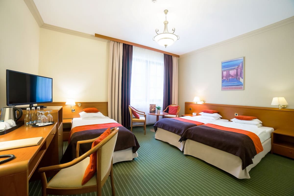 A hotel room with two beds, a desk with a computer, a television, and a chandelier.