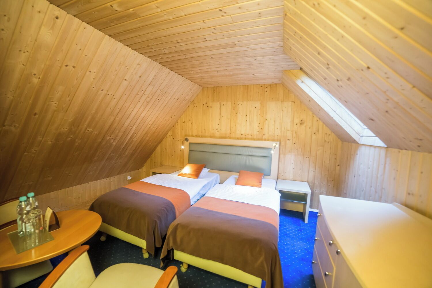 A small, cozy room with two beds, a wooden ceiling, and a skylight.