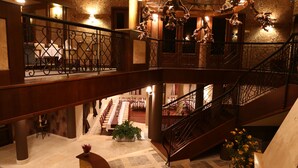 A multi-level hotel lobby with a grand staircase, a dining area, and a reception desk.