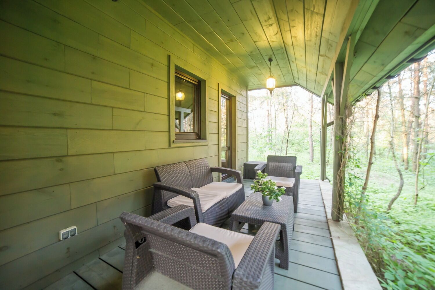 A covered porch with wicker furniture, a small table with a plant, and a view of the surrounding forest.