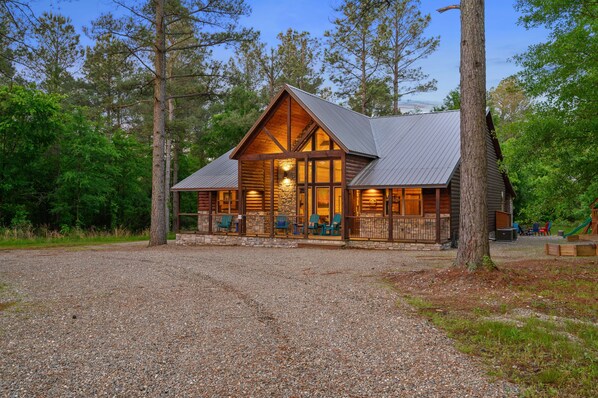A log cabin with a porch, large windows, and a gravel driveway. - Lazy Pine Lodge: 4BR, 4BA, Sleeps 14 (Broken Bow)