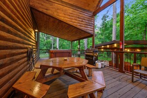 A wooden deck with picnic tables and a grill area, surrounded by a wooden cabin structure. - Lazy Pine Lodge: 4BR, 4BA, Sleeps 14 (Broken Bow)