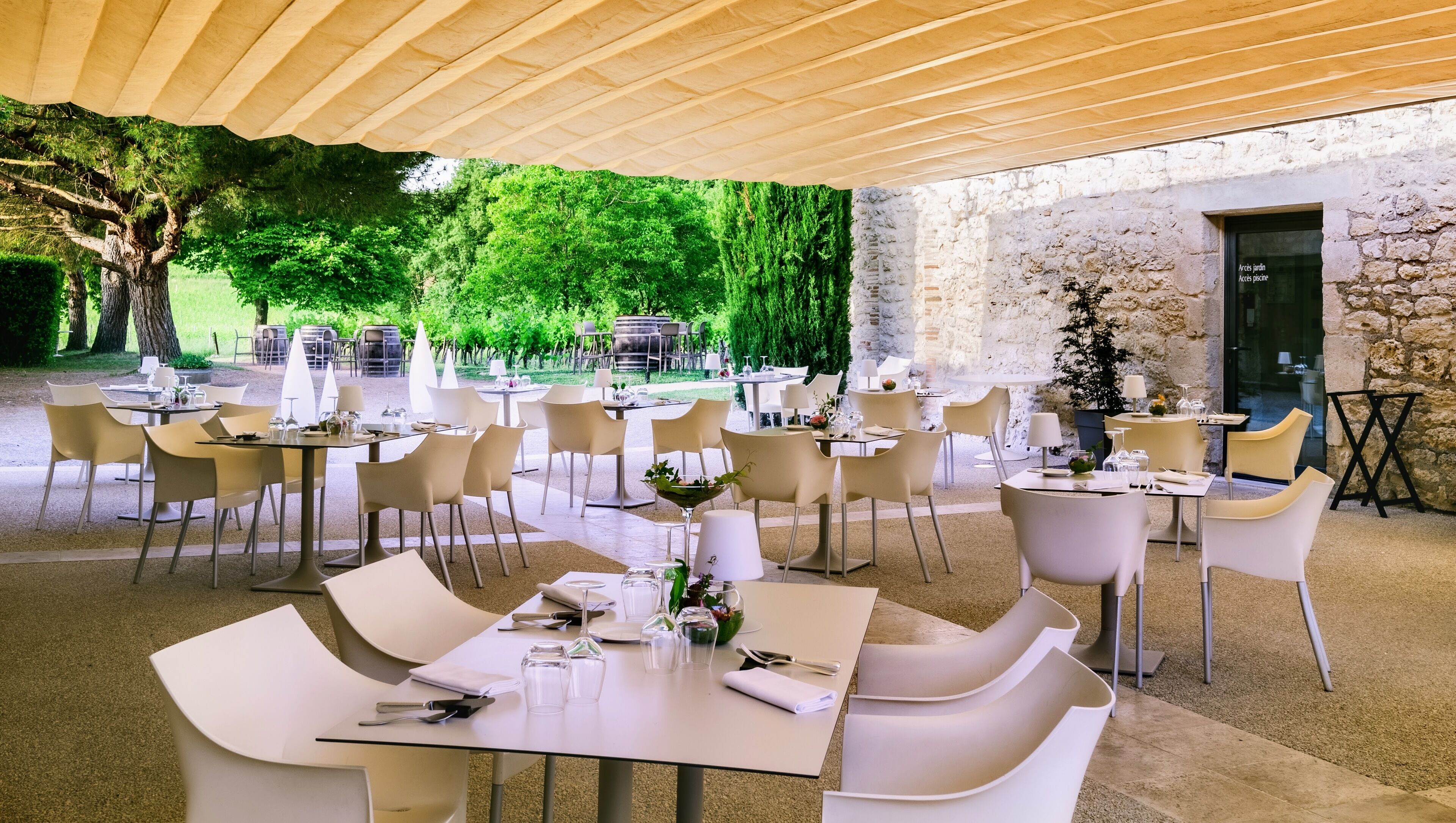 Un espacio exterior para comer con mesas y sillas, un muro de piedra y vistas a un jardín.