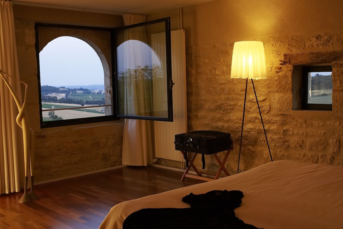 Une chambre d’hôtel avec une grande fenêtre en arc de cercle, un lampadaire, une petite table et un lit.