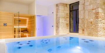 Un área de spa con un jacuzzi, sauna de madera y paredes de piedra.