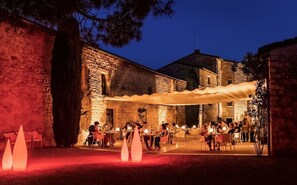 An outdoor dining area with stone walls and tables under a canopy.
