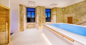 Un spa moderno con pared de piedra, una bañera grande y una puerta de madera.