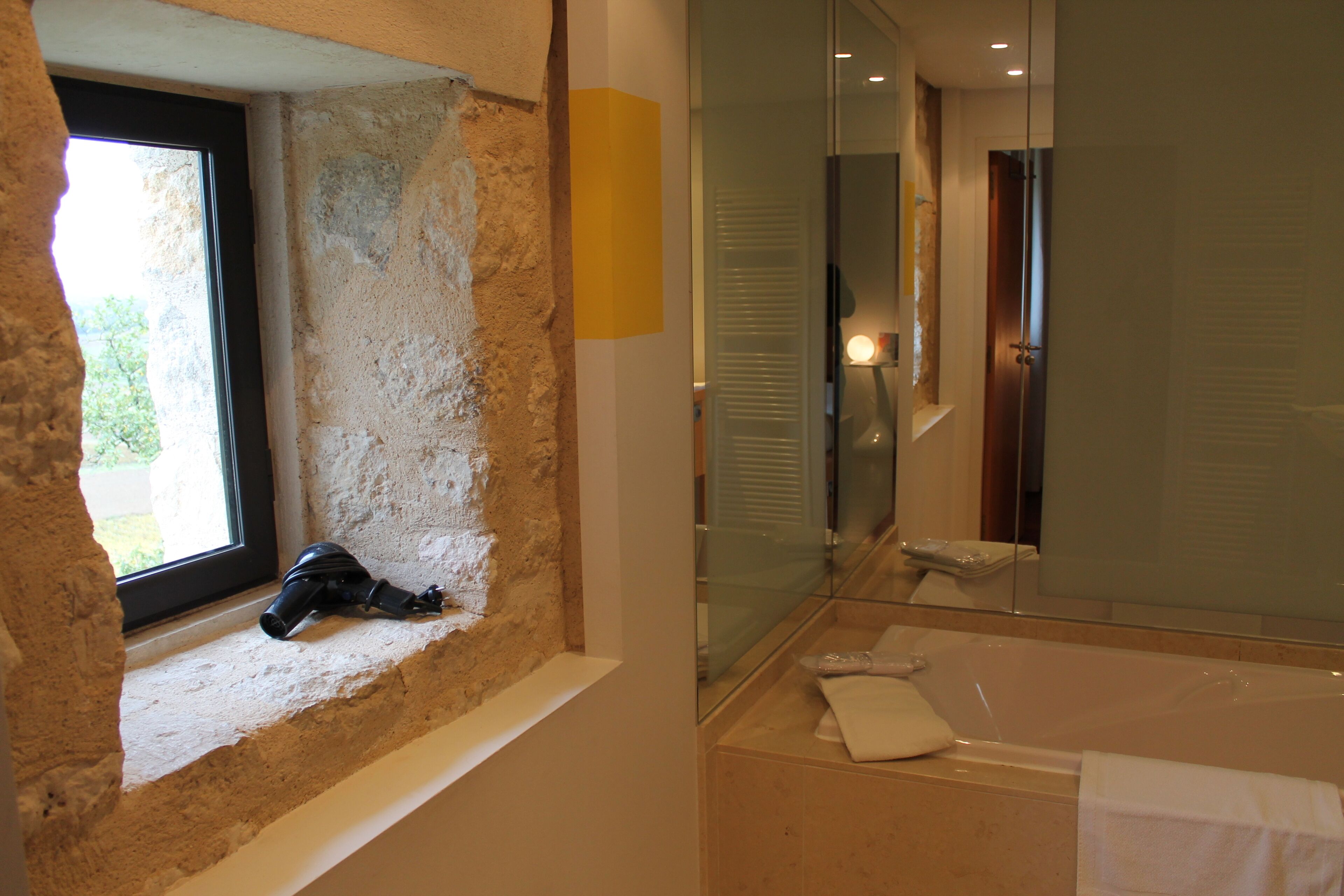 A bathroom with a stone wall, a window, a bathtub, and a mirror.