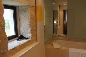 Un baño con pared de piedra, ventana, bañera y espejo.