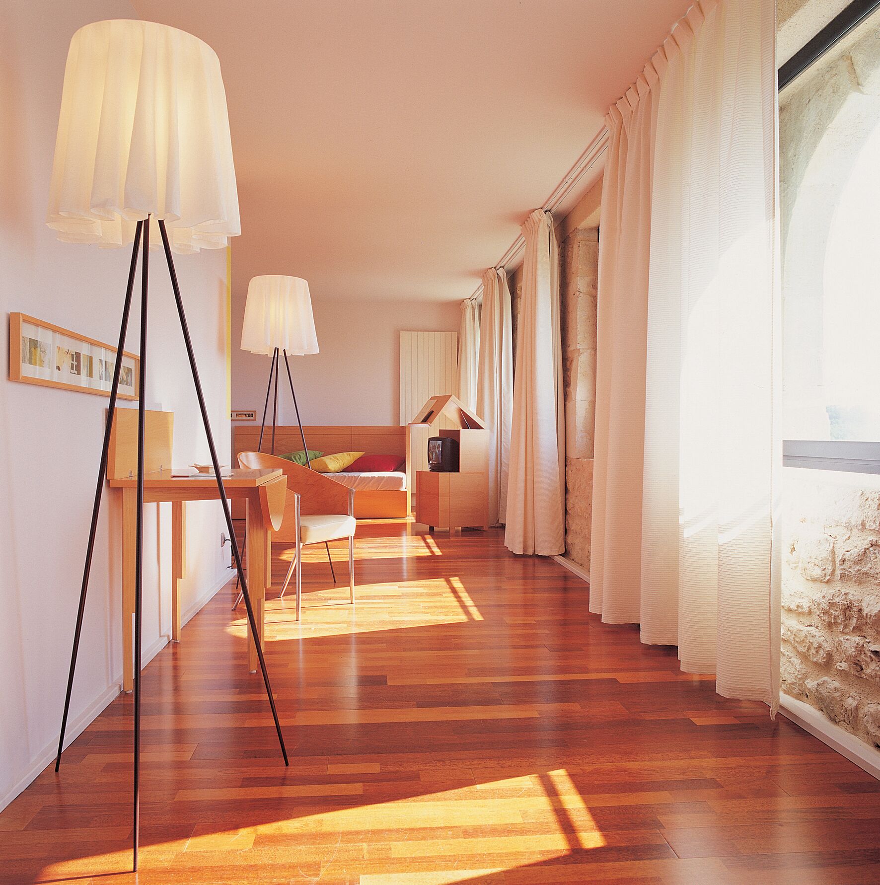 A modern living room with a wooden floor, a dining area with a table and chairs, and a large window with curtains.