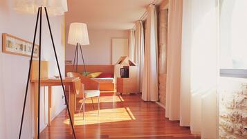 A modern living room with a wooden floor, a dining area with a table and chairs, and a large window with curtains.