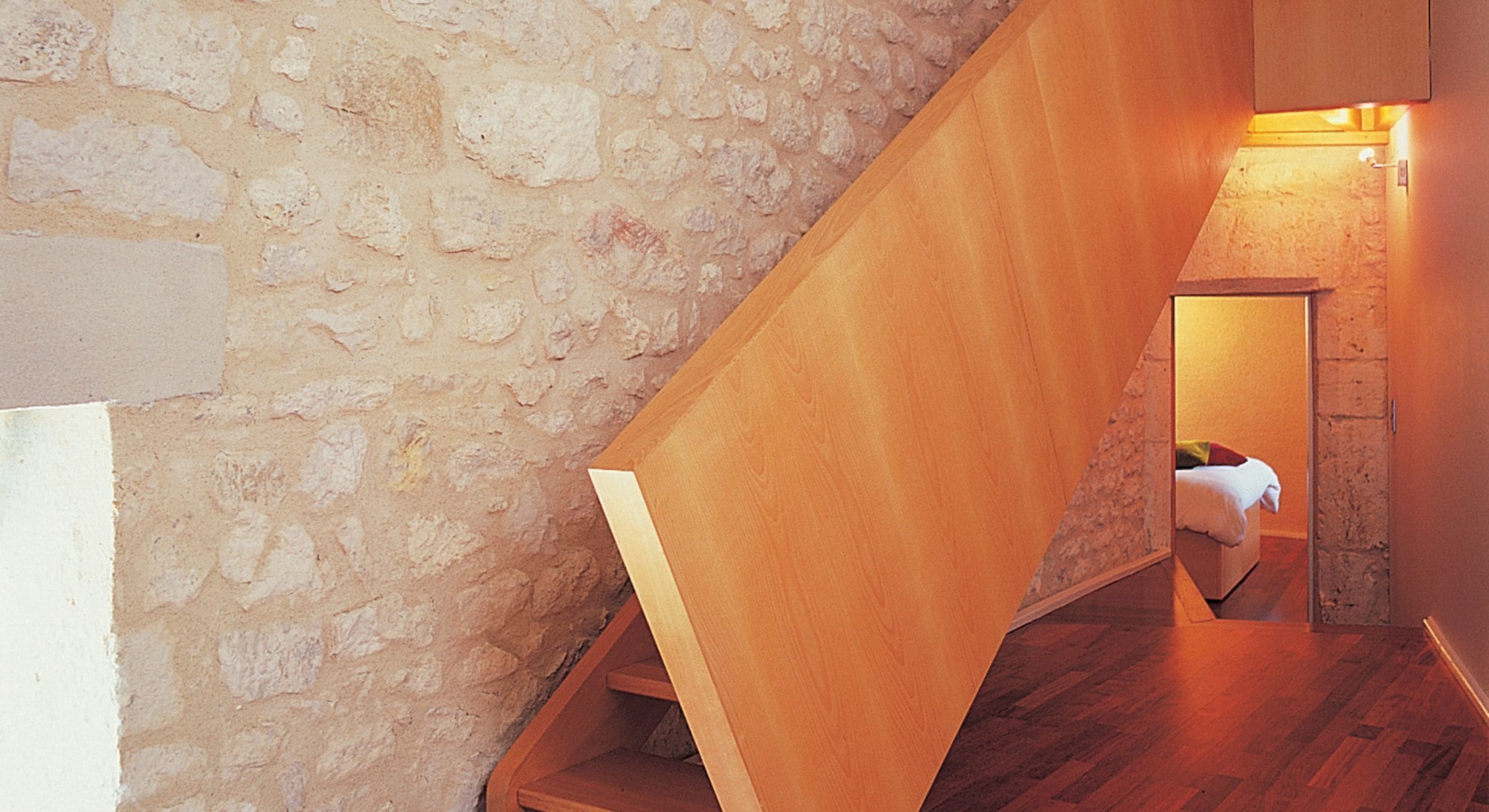 Una escalera de madera con un muro de piedra a un lado y piso de madera.