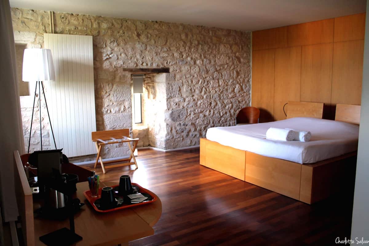 Une chambre avec un lit en bois, un mur en pierre, un bureau avec une lampe et une chaise.