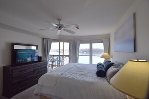 A bedroom with a bed, a ceiling fan, a TV on a dresser, and a view of the outdoors.