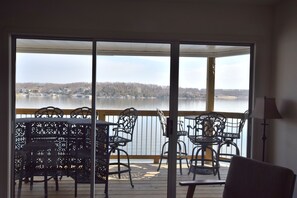 A room with a view of a lake, a balcony with outdoor furniture, and a sliding glass door.