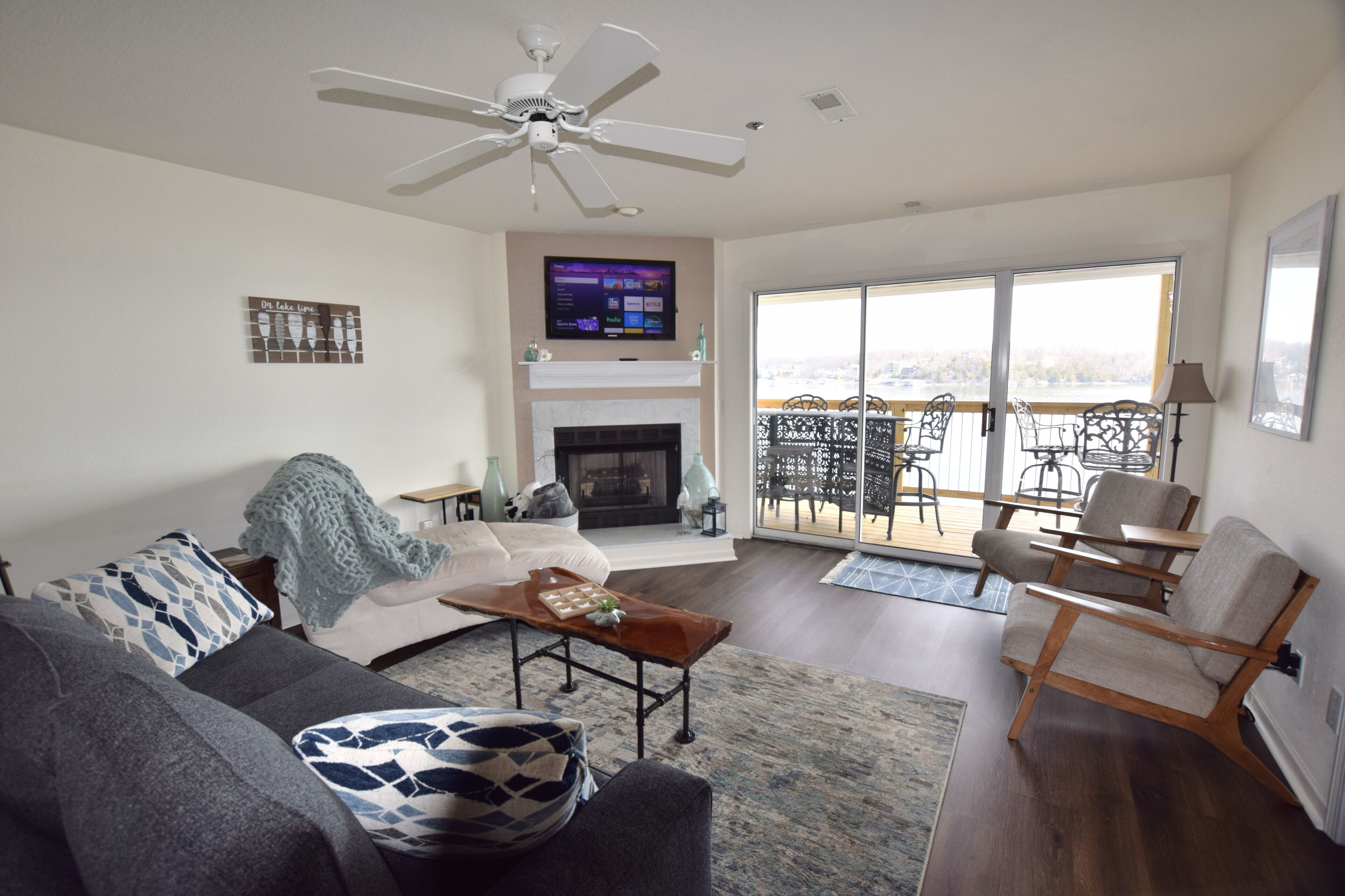 Een woonkamer met een bank, salontafel, open haard, televisie en een balkon met tuinmeubilair.