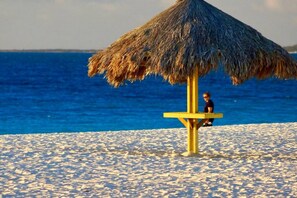 A beach umbrella with a thatched roof on a sandy beach.