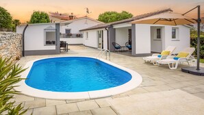 Une piscine avec une terrasse carrelée, un patio couvert doté de chaises longues et un mur en pierre.