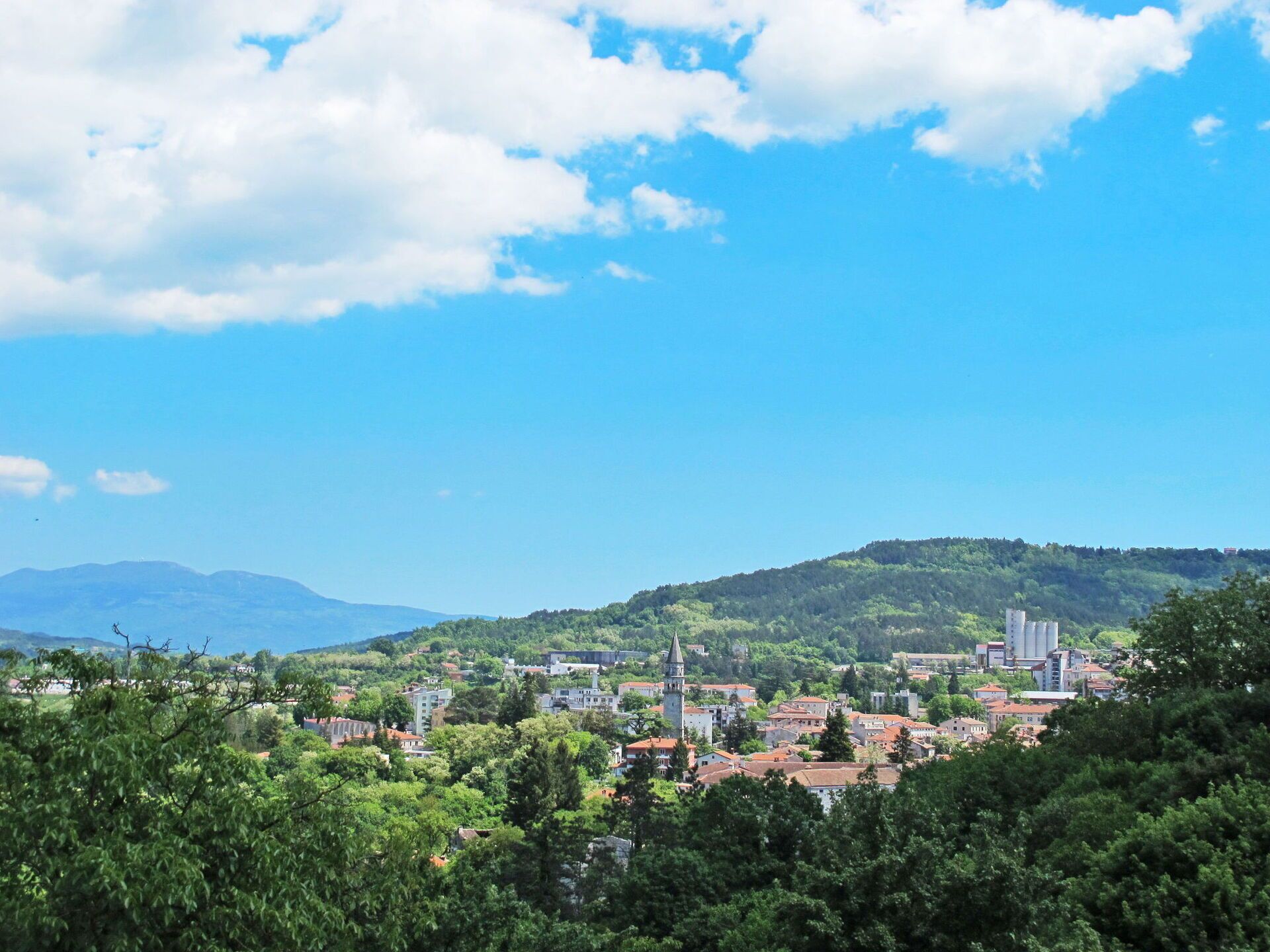 A town with a prominent church tower, surrounded by greenery and buildings with red roofs.