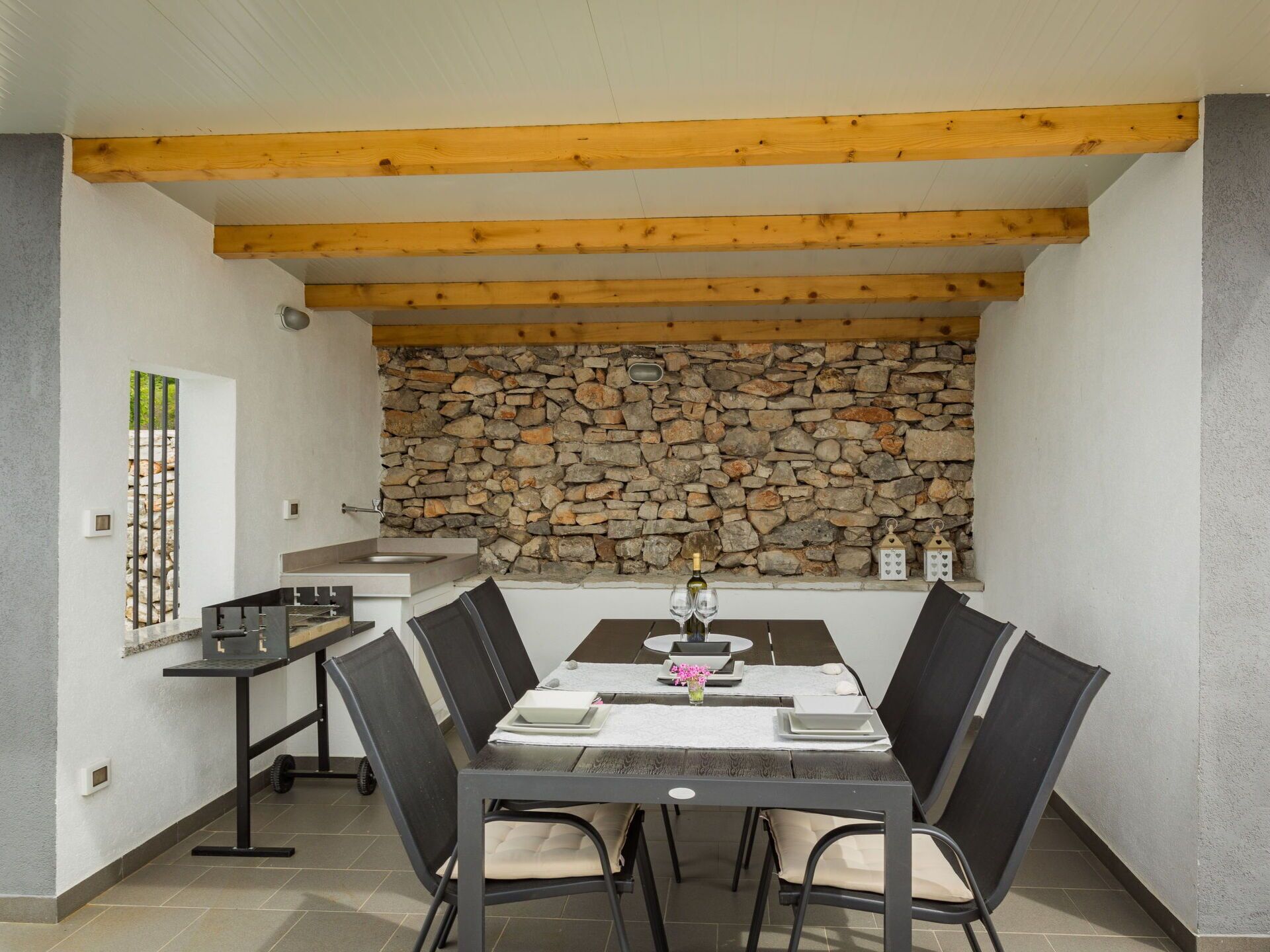 A dining area with a stone wall, wooden beams, and a modern kitchen in the background.