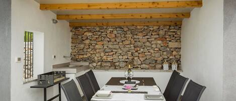 A dining area with a stone wall, wooden beams, and a modern kitchen in the background.
